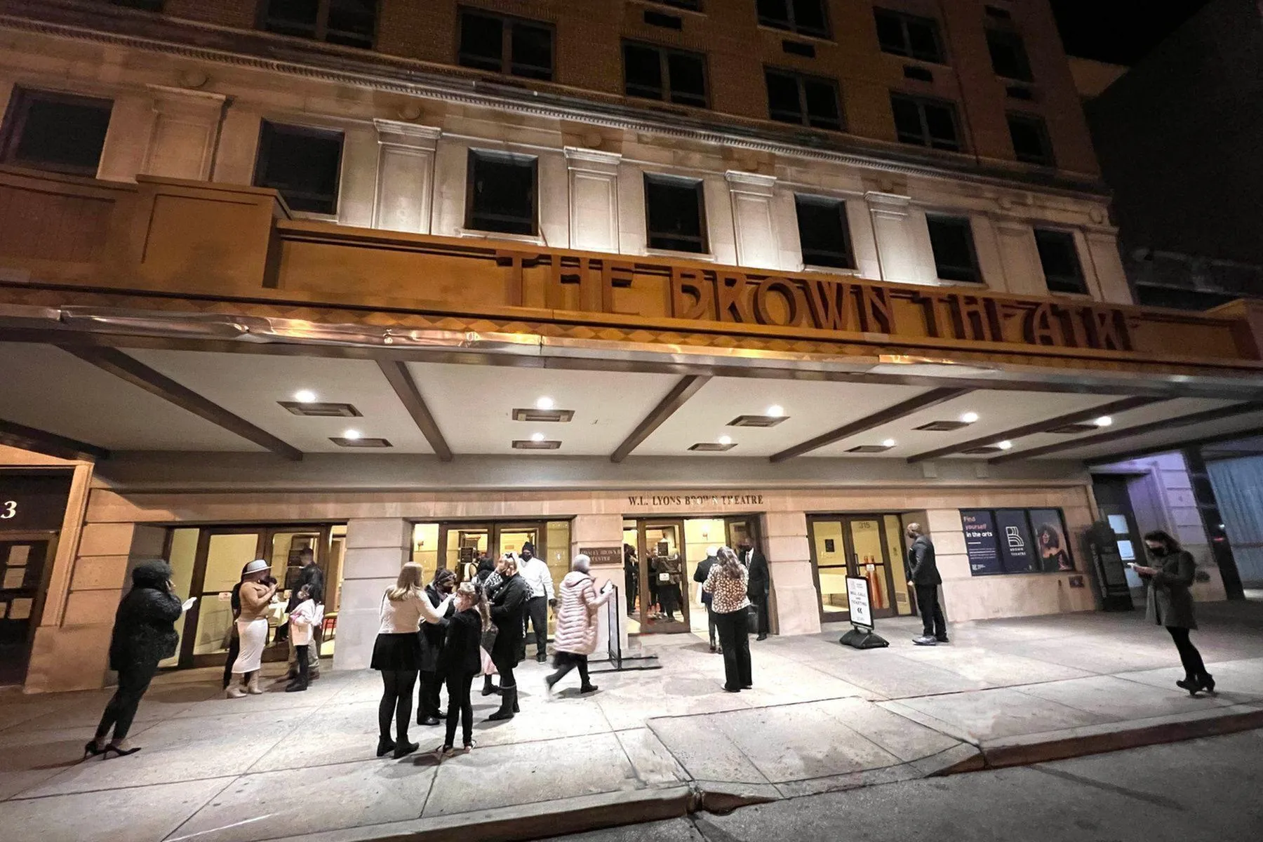 Elegant theatre entrance illuminated at night with people gathering under the marquee.