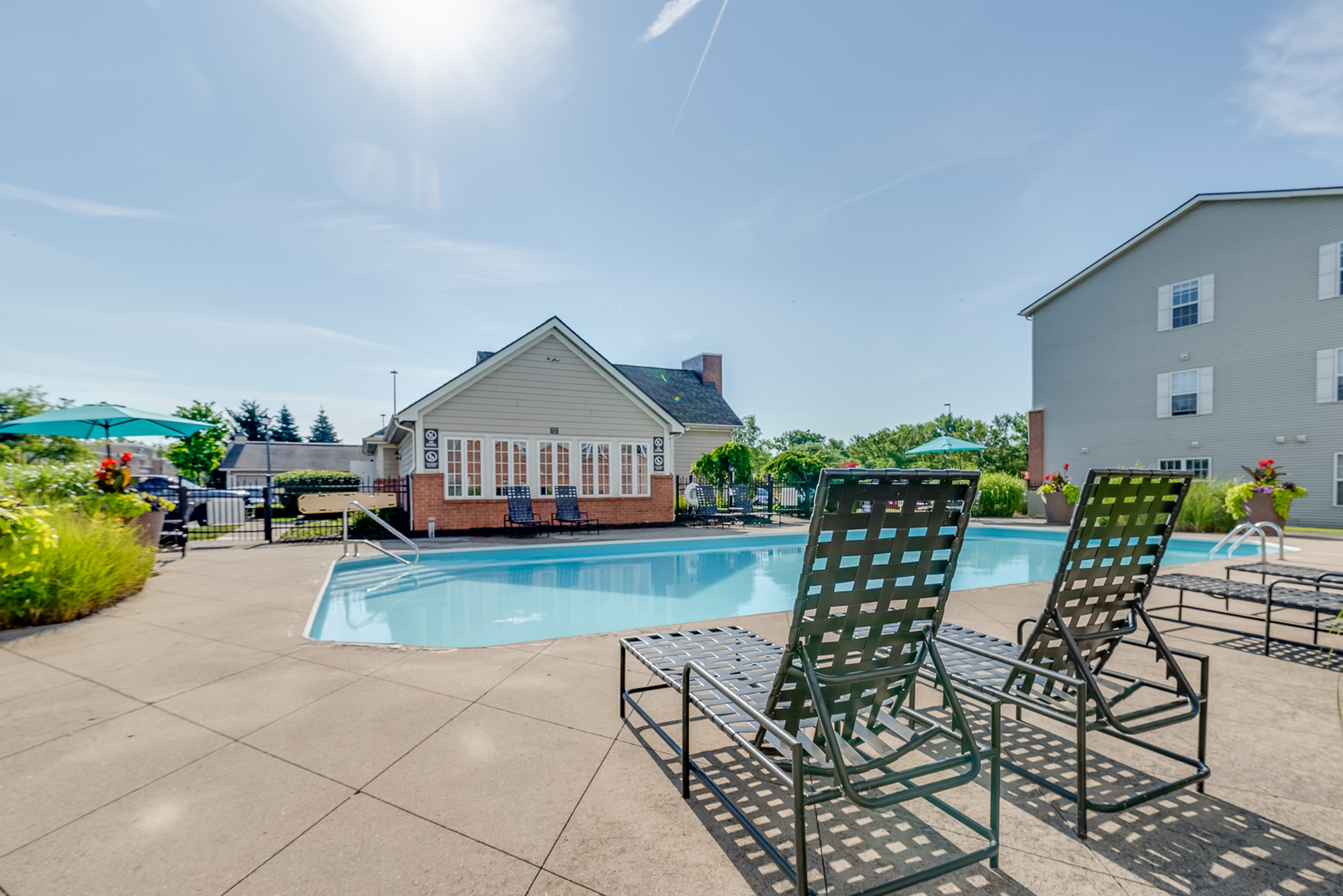 Inviting outdoor pool area with sun loungers and modern clubhouse, perfect for relaxation and leisure.