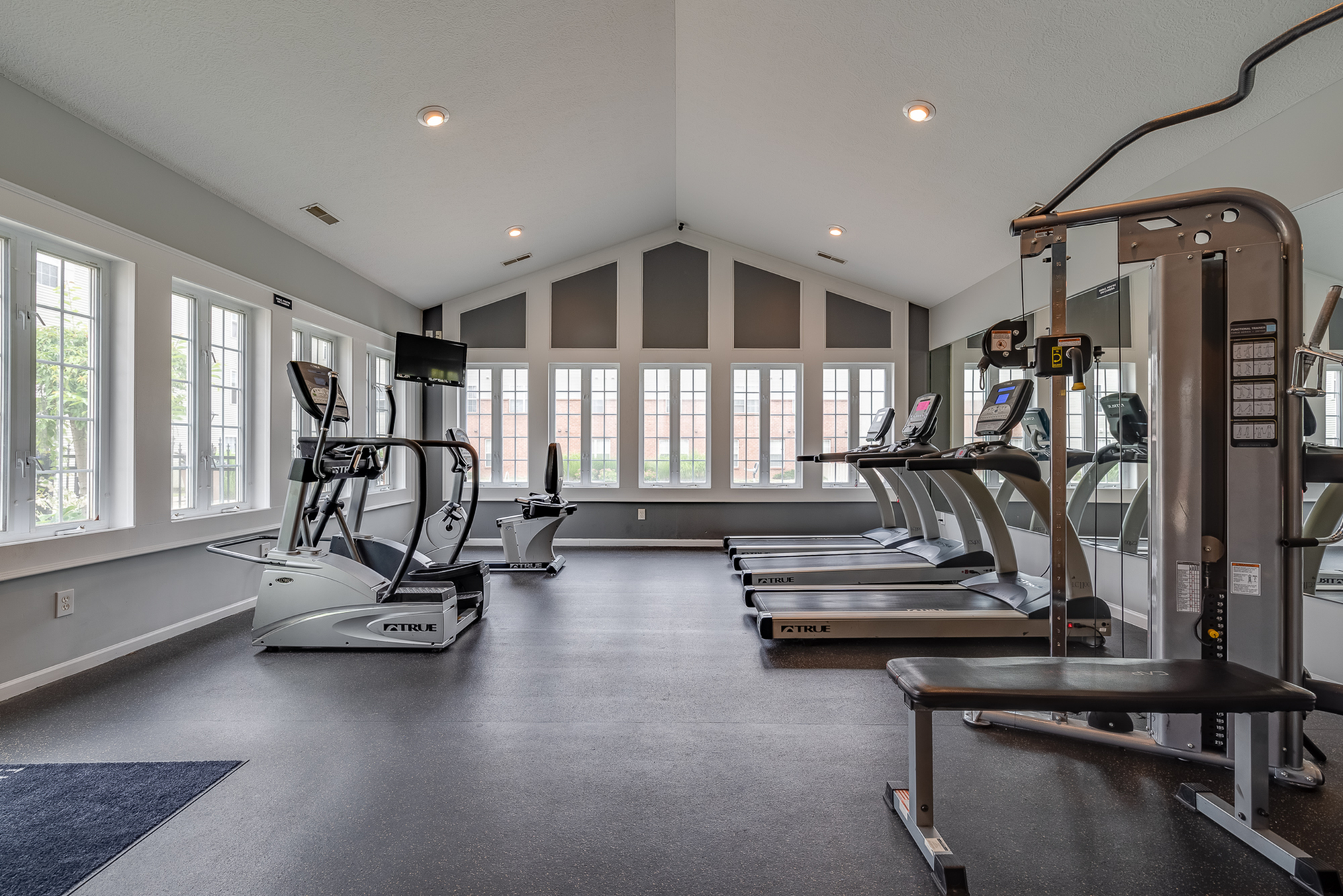 Bright and spacious apartment gym featuring modern exercise equipment and large windows offering natural light.