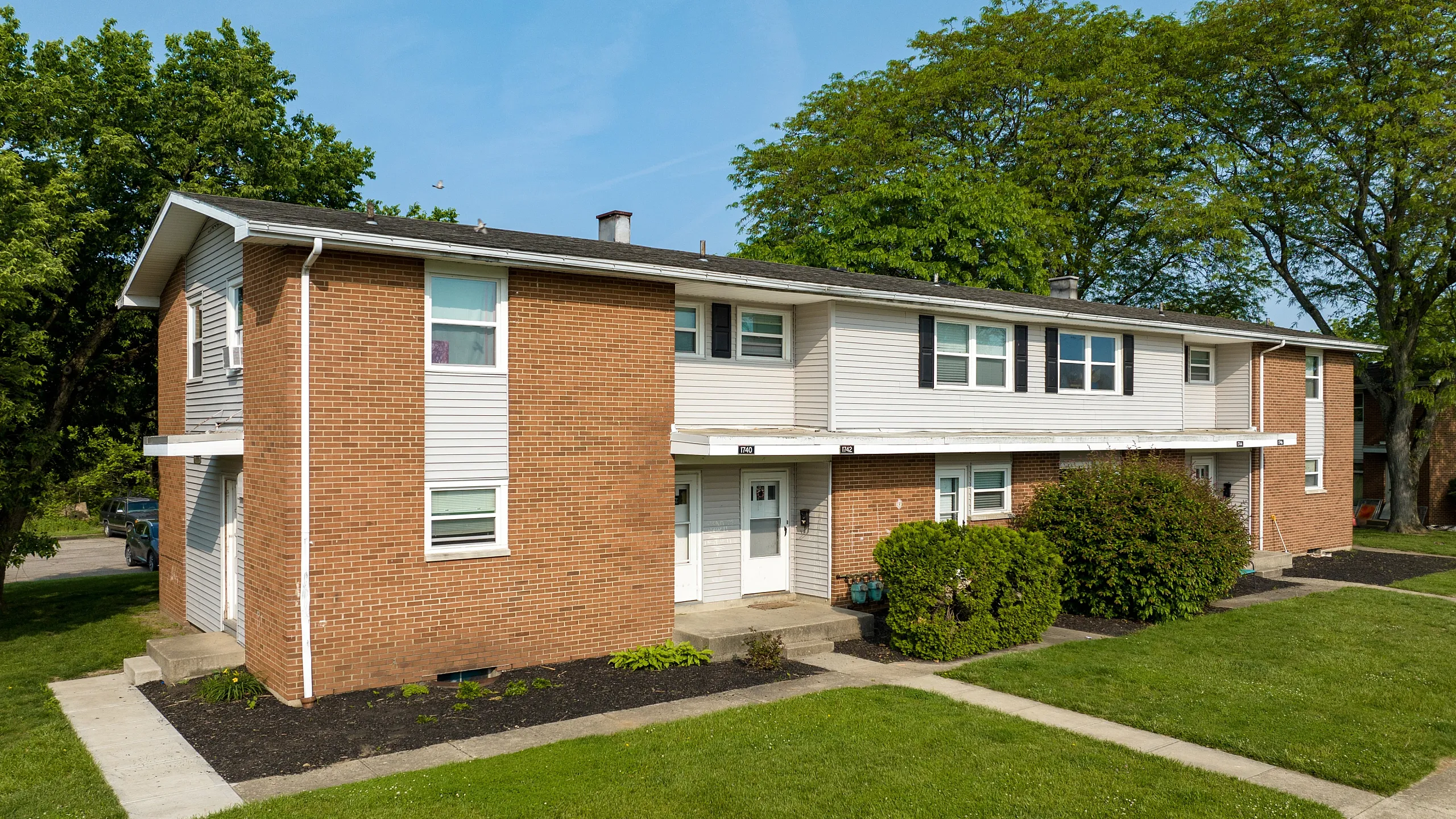 A welcoming two-story brick apartment building surrounded by lush greenery on a sunny day.