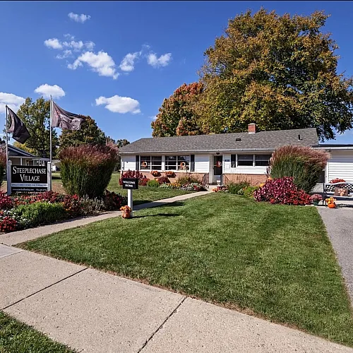 Beautiful home in Steeplechase Village with vibrant garden and flags under a clear blue sky.