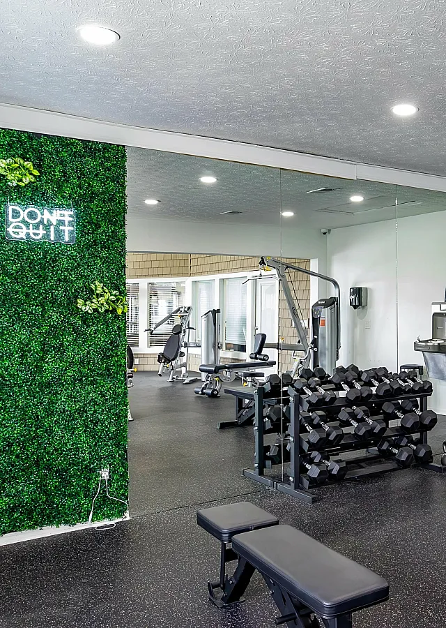 Contemporary gym with neon 'Don't Quit' sign, mirrored walls, and free weights.
