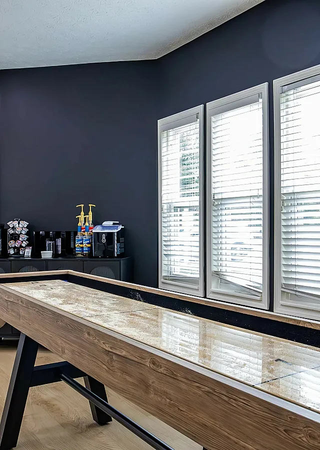 Chic entertainment room with shuffleboard table and modern decor in a sunlit space.