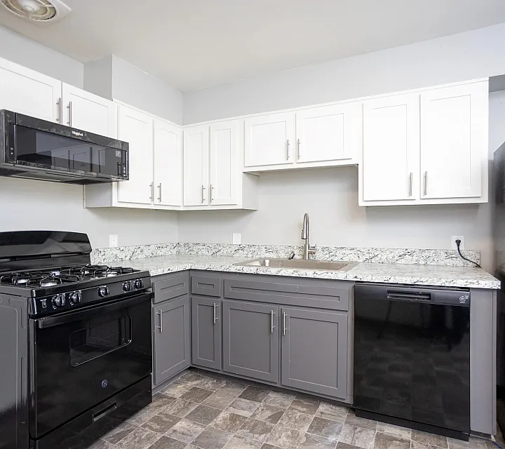 Modern kitchen with sleek black appliances, granite countertops, and white and gray cabinetry.