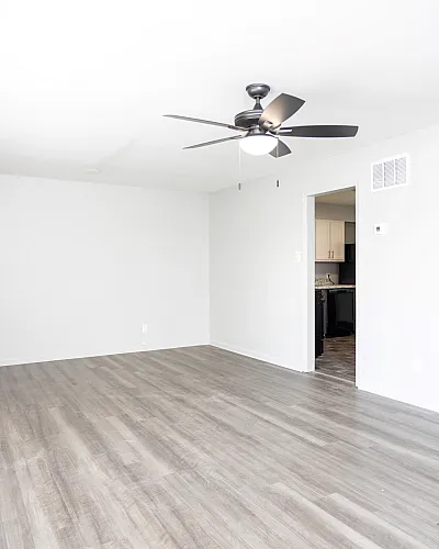 Bright and airy living room with sleek wooden flooring, modern ceiling fan, and open access to the kitchen.