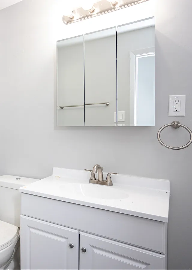 Chic bathroom with white vanity, mirror cabinet, and large window with blinds.