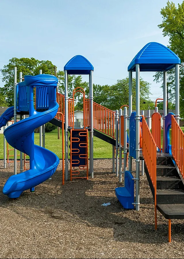 Colorful playground set with slide and climbing structure in a sunny park environment.