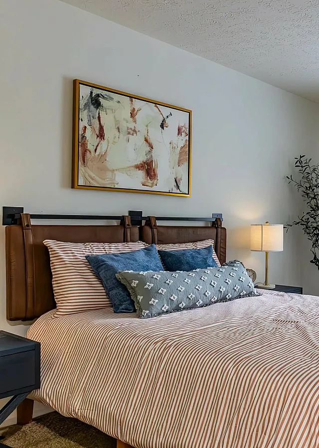 Inviting bedroom with a comfortable bed, stylish artwork, and natural light streaming through a large window.