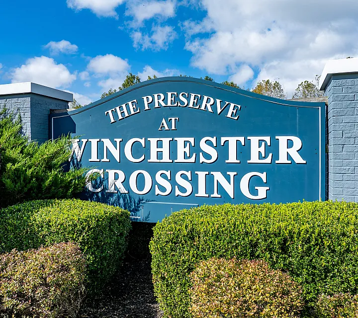 Beautiful sign for The Preserve at Winchester Crossing surrounded by lush greenery and a clear blue sky.