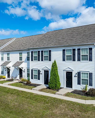 Bright and inviting townhome with white siding and black shutters, set against a vibrant blue sky.