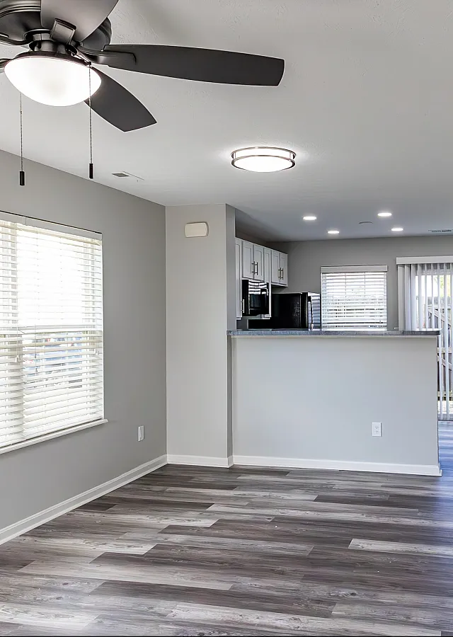 Bright and open living area with modern flooring, ceiling fan, and a view into the kitchen.