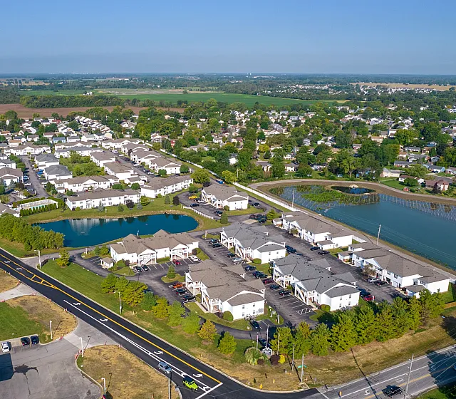 Aerial view of a serene residential community with neatly arranged houses, lush greenery, and scenic water features.