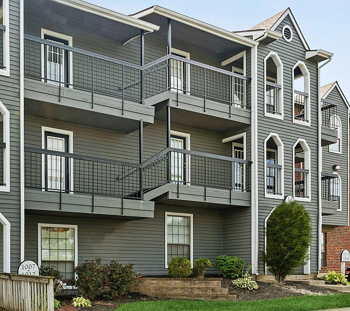 Charming three-story apartment building with gray siding, white trim, and spacious balconies.