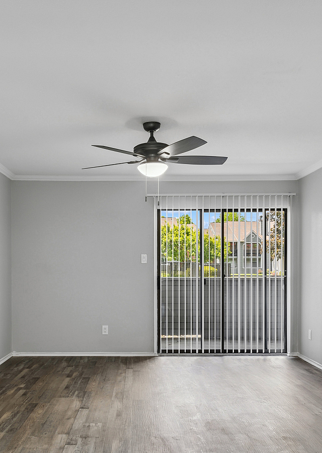 Bright, modern living room with wood flooring, ceiling fan, and large sliding glass door to balcony.
