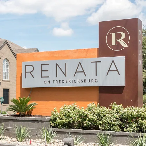 Welcoming entrance of Renata on Fredericksburg with modern signage amidst lush landscaping and contemporary apartments.