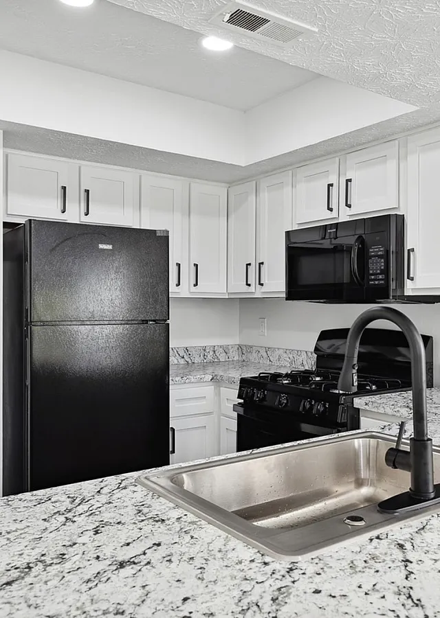 Modern kitchen with elegant granite countertops, sleek black appliances, and pristine white cabinetry.