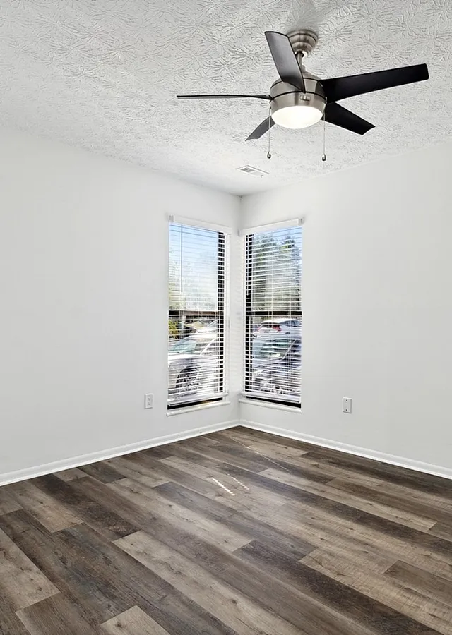 Bright, minimalistic room featuring elegant wood flooring, large windows with blinds, and a modern ceiling fan.