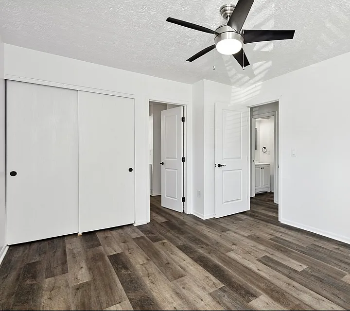 Bright and modern room with sleek wooden flooring, elegant ceiling fan, and ample closet space showcasing contemporary design.