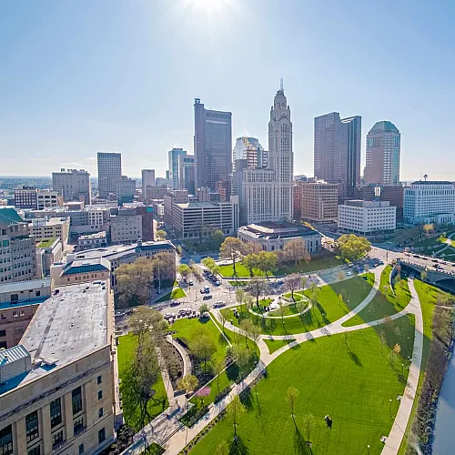 Stunning cityscape view showcasing a vibrant downtown skyline with lush green parks and a serene riverfront under a clear blue sky.