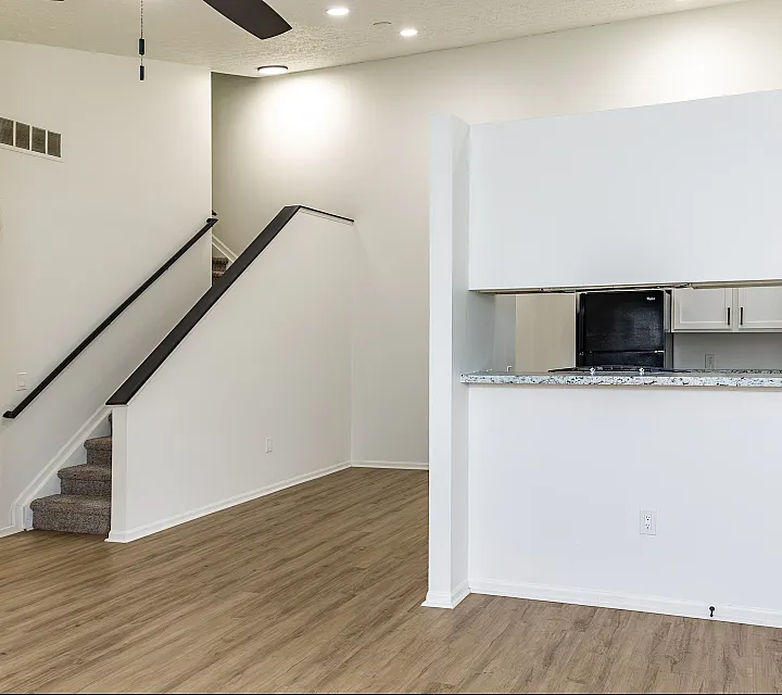 Modern apartment interior with sleek kitchen featuring granite countertops, open floor plan, and elegant staircase.