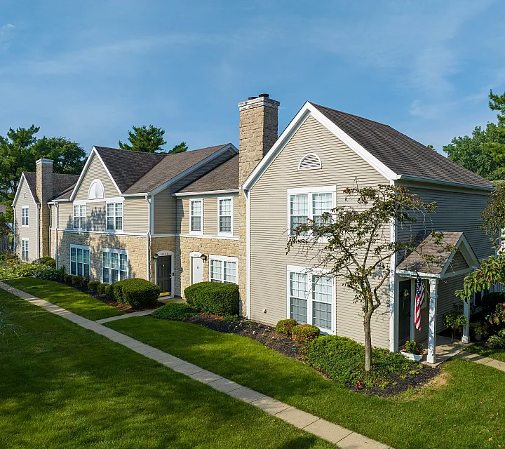 Charming two-story townhouse with elegant stone accents and manicured lawns basking under a clear blue sky.