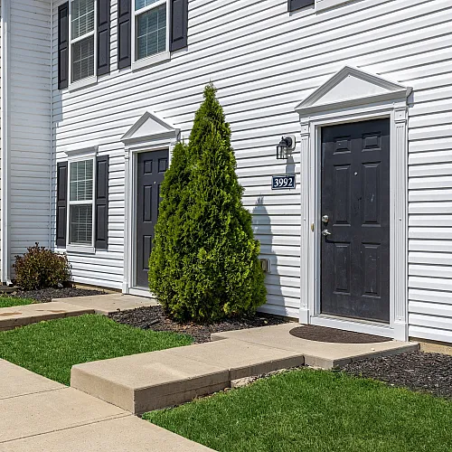 Charming townhouse exterior with modern white siding, lush green landscaping, and inviting entryways.