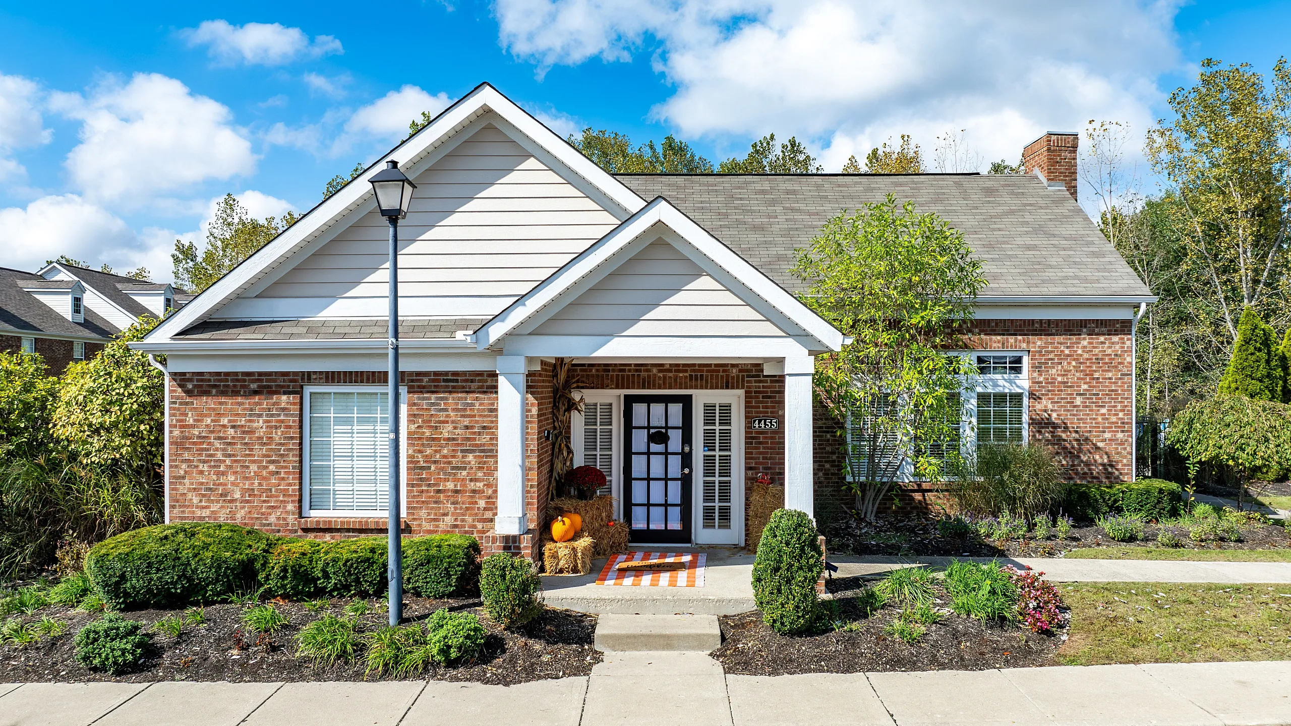 Charming brick-front house with a welcoming porch, nestled amid vibrant landscaping under a bright blue sky.