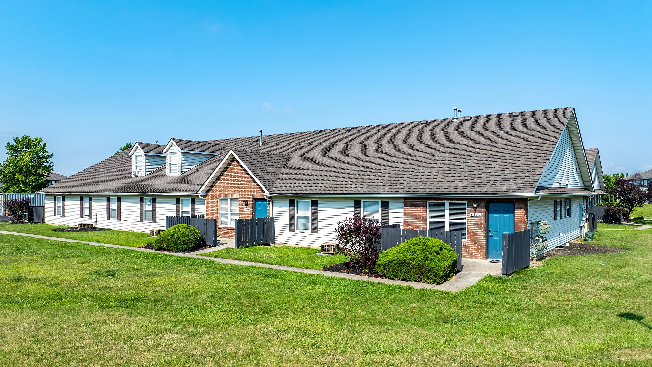 Charming suburban duplex with brick accents, surrounded by lush green lawns and a vibrant sky.