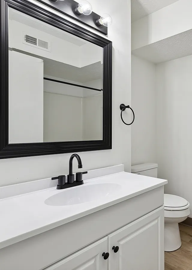 Modern bathroom featuring a sleek white vanity, elegant black-framed mirror, and stylish light fixtures, offering a bright and clean space.
