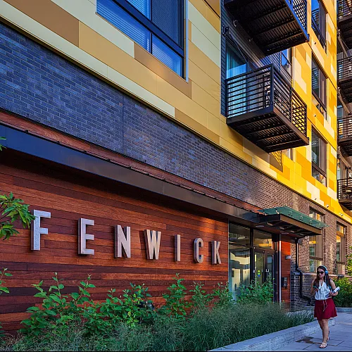Vibrant yellow modern apartment building with unique architectural design, featuring private balconies and lush landscaping.