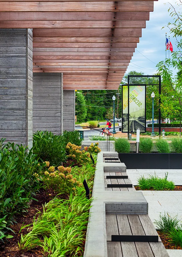 Modern outdoor urban space featuring lush greenery, wooden benches, and a contemporary walkway under a stylish pergola.