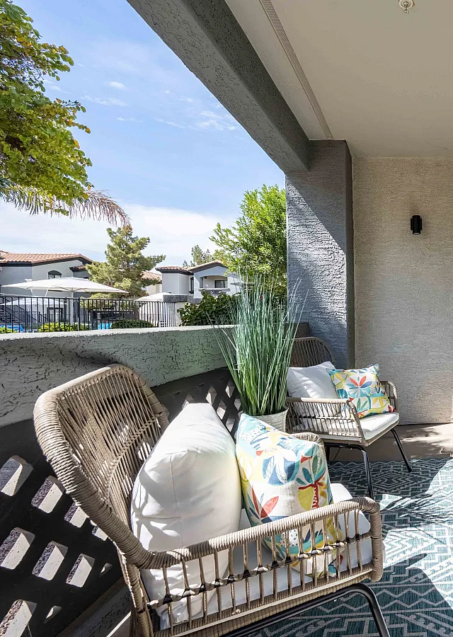 Charming apartment patio with stylish wicker chairs, vibrant cushions, and a lush potted plant, perfect for relaxing.