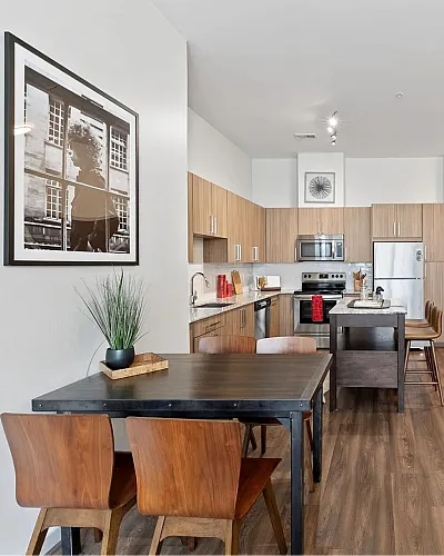 Modern apartment kitchen with sleek wooden cabinets, stainless steel appliances, and a cozy dining area with artistic decor.