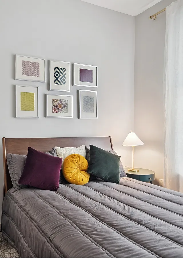 Cozy bedroom featuring a stylish bed with colorful pillows, elegant wall art, and a view into a chic living area with modern decor.