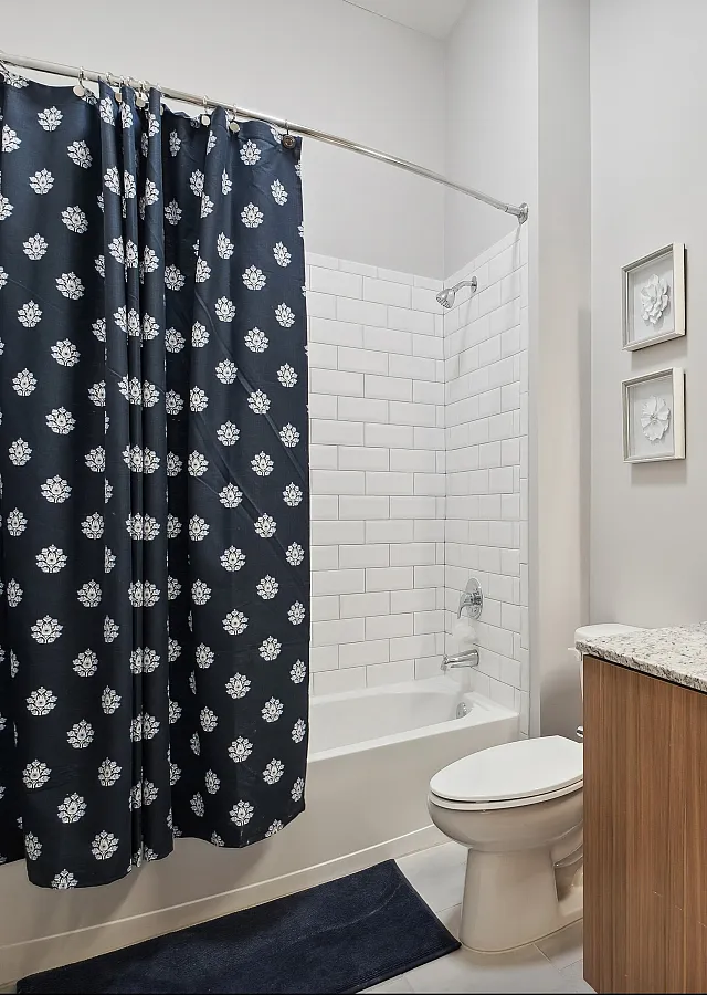 Modern bathroom featuring a sleek granite countertop, elegant white tiles, and a chic navy shower curtain with a floral pattern.