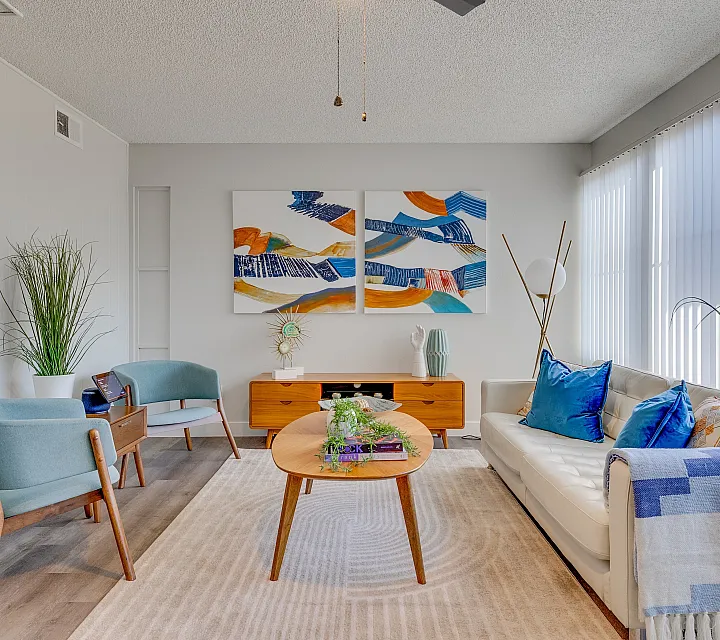Modern living room with elegant decor featuring blue-accented furniture, abstract wall art, and ample natural light.