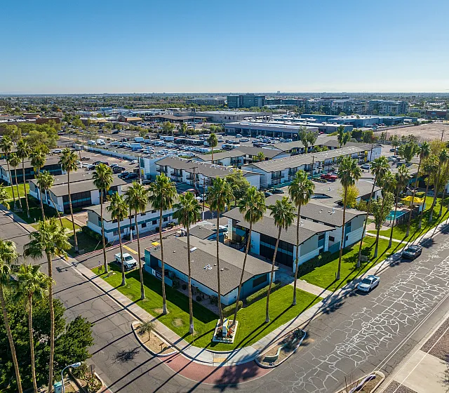 Aerial view of a modern apartment complex surrounded by lush green lawns and tall palm trees, offering a refreshing urban oasis.