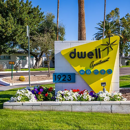 Vibrant sign for Dwell Apartment Homes with a modern design, surrounded by manicured landscaping and colorful flowers.