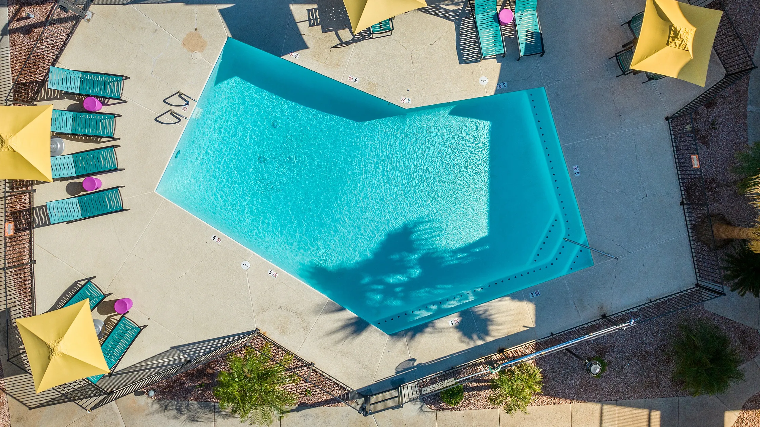 Inviting aerial view of a stylish outdoor pool area featuring vibrant lounge chairs and yellow umbrellas, perfect for relaxation and leisure.