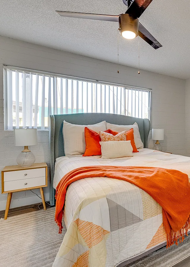 Inviting bedroom with large windows, featuring a comfortable bed with stylish orange accents and modern decor.