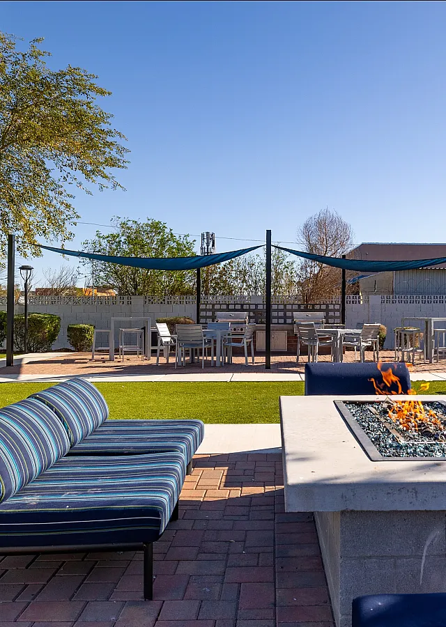Inviting outdoor lounge area featuring a modern fire pit, stylish seating, and lush green surroundings under a clear blue sky.