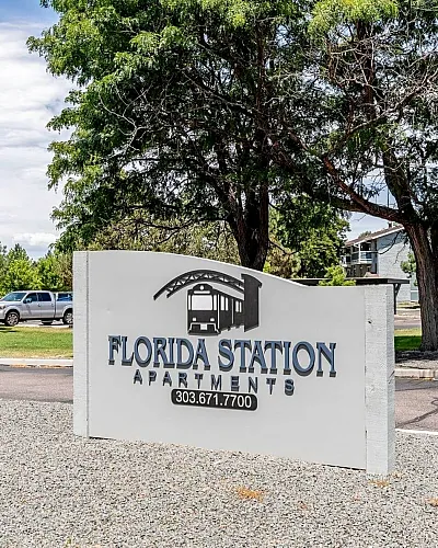 Inviting entrance sign for Florida Station Apartments surrounded by lush greenery and ample parking.