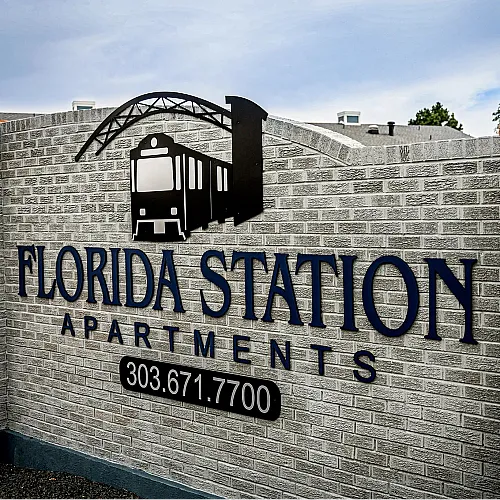 Elegant entrance sign for Florida Station Apartments featuring a modern train motif on a brick wall backdrop.