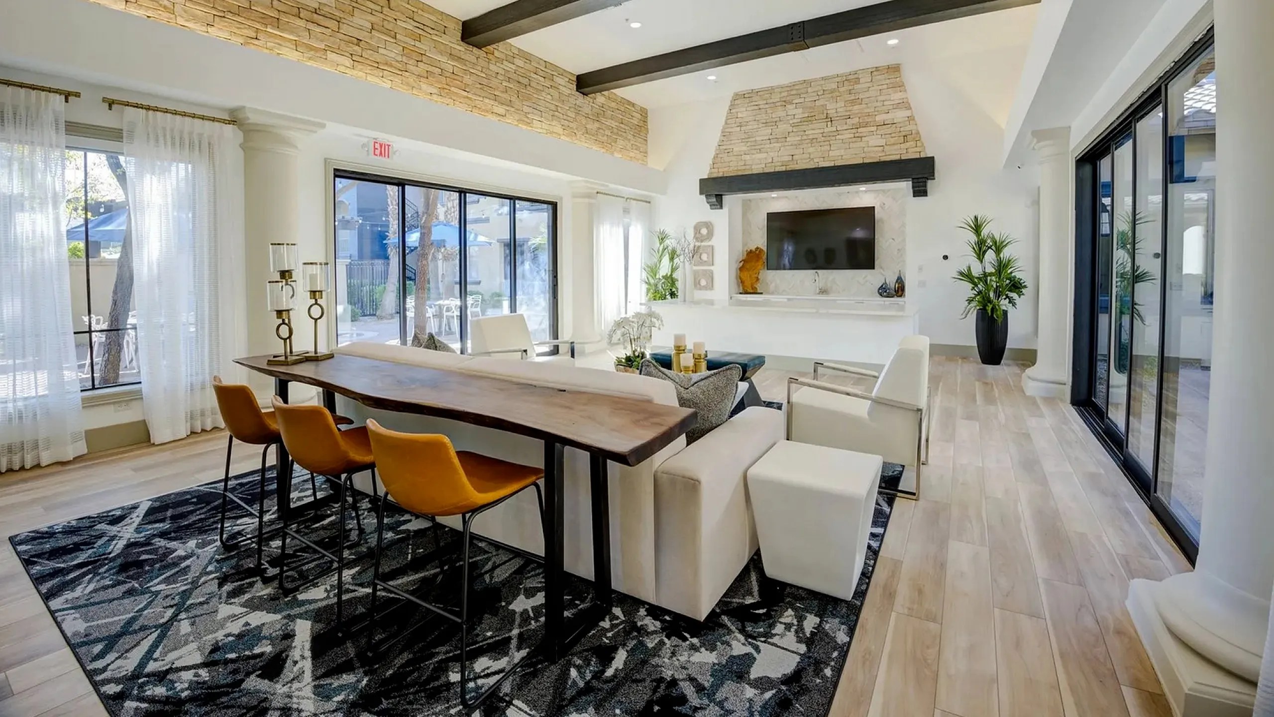 Elegant living room with vaulted ceilings, stone accents, and modern furniture. Bright space featuring a cozy seating area, expansive windows, and a stylish dining table with golden chairs.