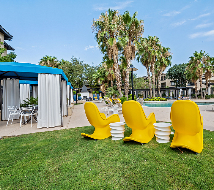 Vibrant outdoor pool area with lush palm trees, modern yellow lounge chairs, and shaded cabanas creating a luxury resort ambiance.