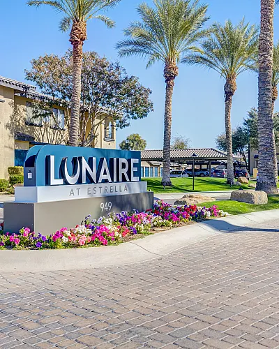 Inviting entrance of LUNAIRE AT ESTRELLA with elegant landscaping, vibrant flowers, and majestic palm trees, promising luxurious living.