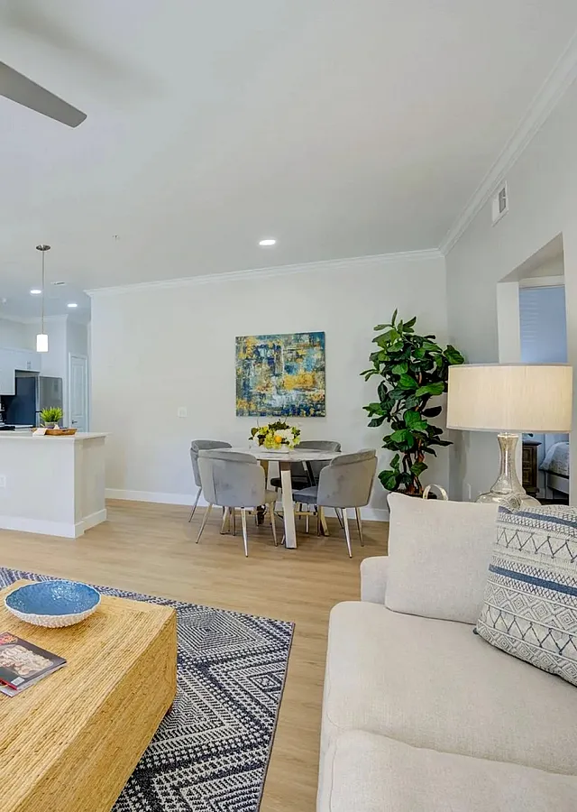Bright, modern living room with cozy seating, stylish rug, and elegant decor opening to a sleek open-plan kitchen and dining area with vibrant artwork.
