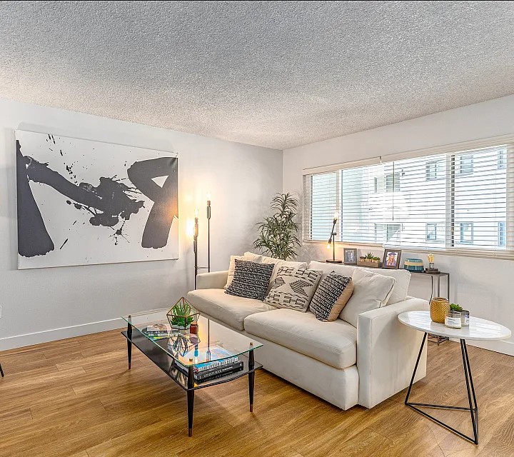 Contemporary living room showcasing elegant hardwood floors, a plush white sofa, and stylish abstract wall art, highlighted by ample natural light from large windows.