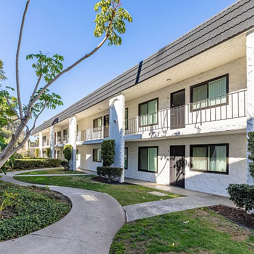 Charming apartment complex with lush landscaping, featuring a beautifully maintained pathway leading to modern, sunlit units.