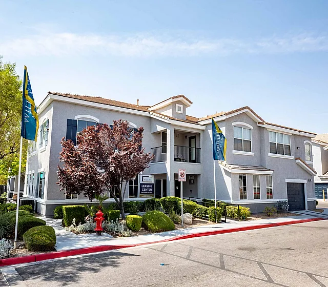 Charming apartment complex with lush landscaping, modern design, and welcoming leasing center set under a clear blue sky.